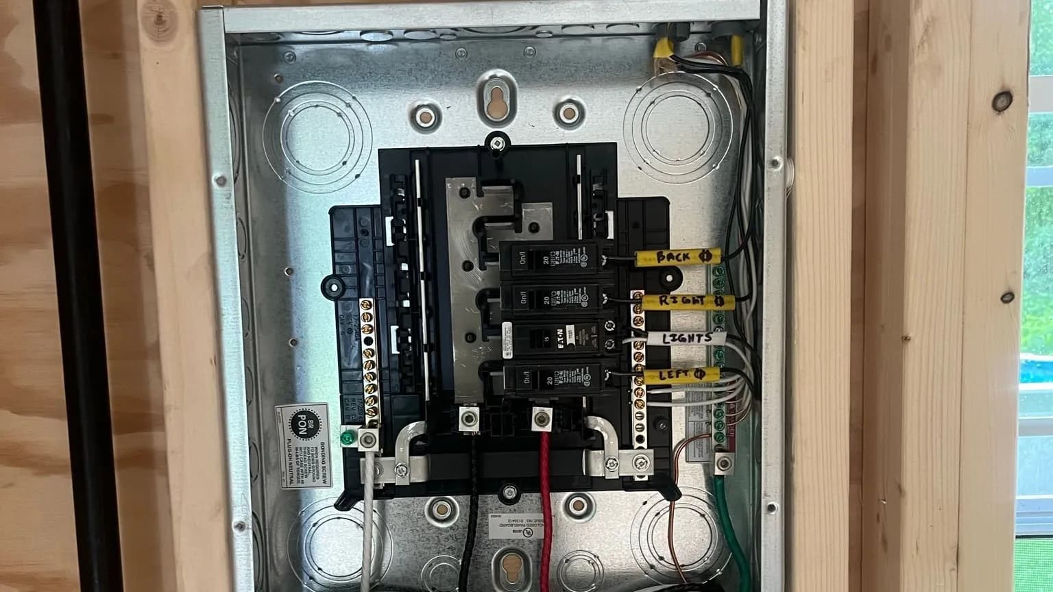 An open Eaton subpanel with its cover off, set between wood studs, with four breakers wired in and the wires tagged with handwritten labels reading Back, Right, Lights, and Left.