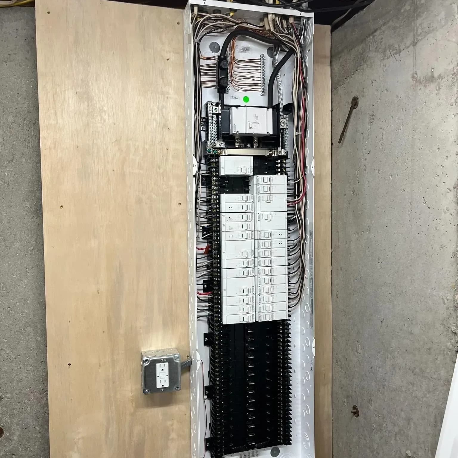 An open breaker panel with the cover off on a plywood backboard, neatly dressed wires running to two long rows of white AFCI breakers and black breakers below them.