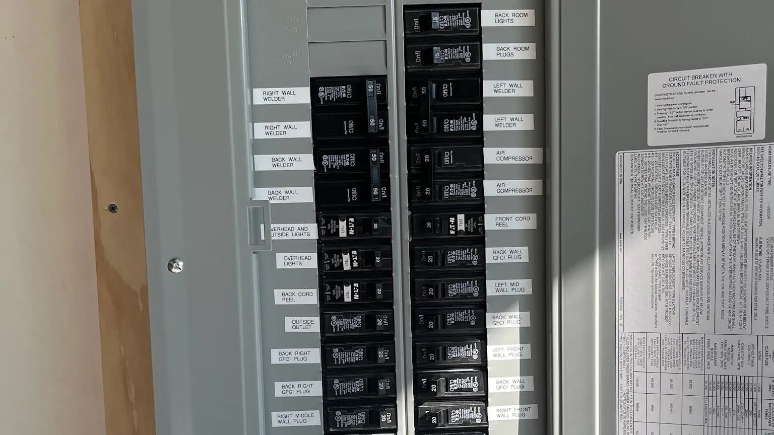 Rows of labeled Eaton circuit breakers, including GFCI breakers, feeding welder, air compressor, cord reel and lighting circuits in a gray panel with printed circuit labels.