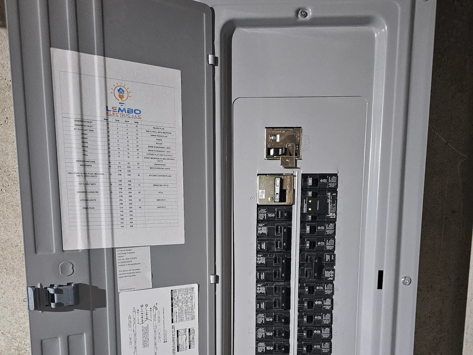 An open breaker panel with a Lembo Electric typed circuit directory on the door, a main breaker, a generator interlock plate and numbered branch breakers.