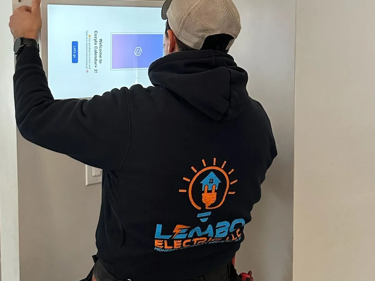A Lembo electrician in a branded hoodie mounts a flush touchscreen display on a white wall.