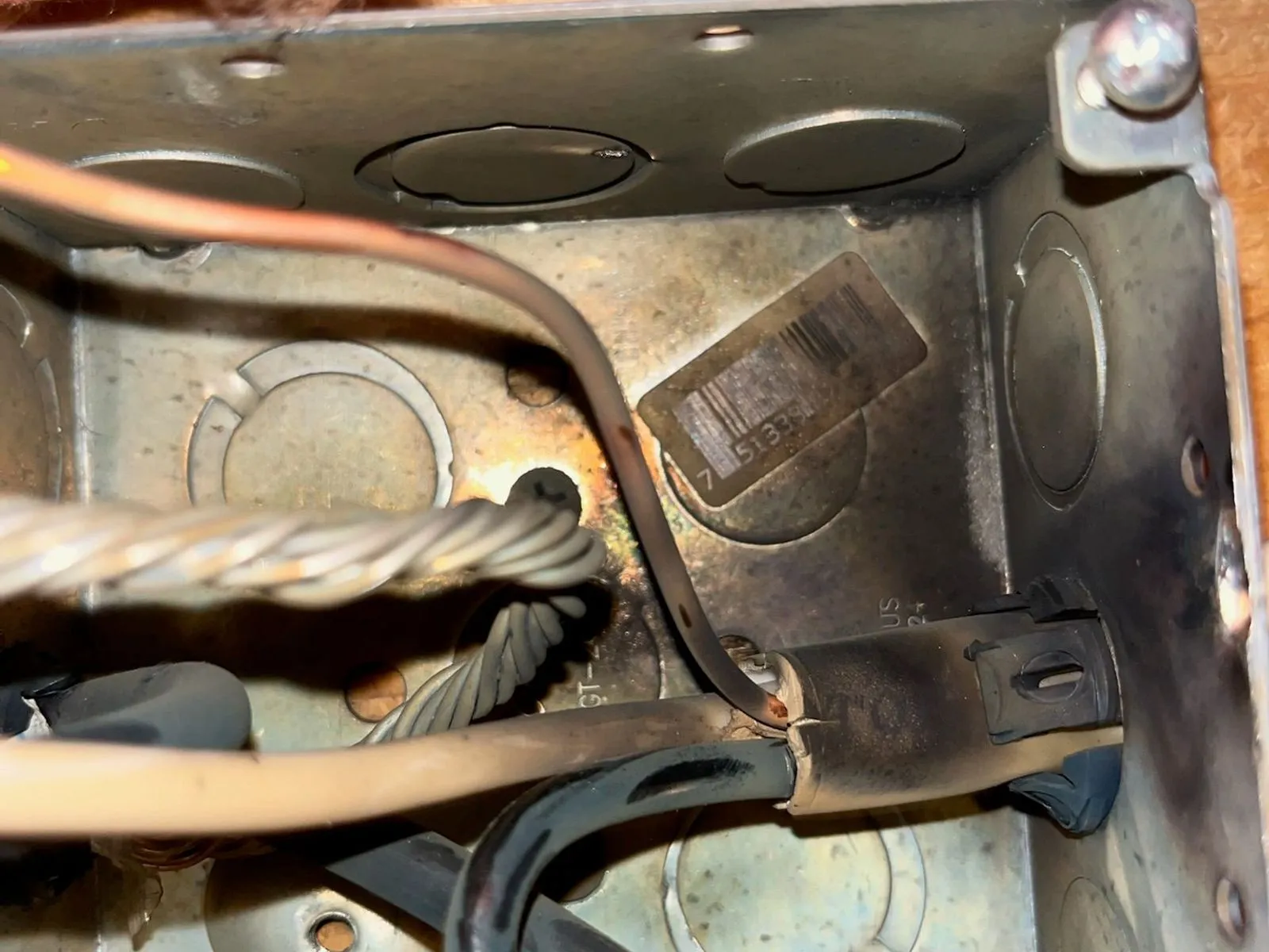 Inside a metal junction box, blackened heat-scorched cable insulation and a soot-stained interior sit below pink insulation, the mark of an overheated connection.