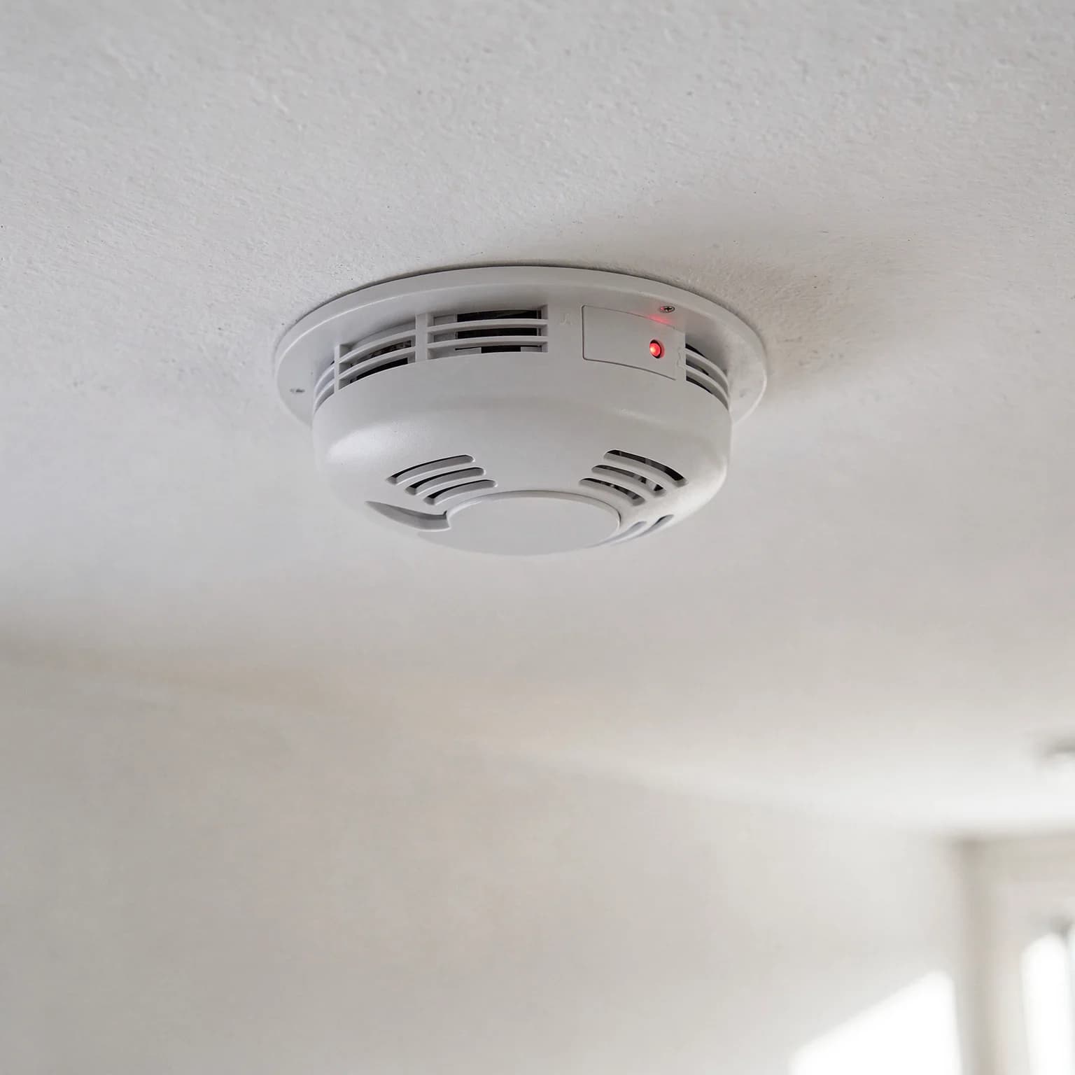 A white ceiling-mounted smoke and carbon monoxide detector with a small red status light in a Lawrence home.