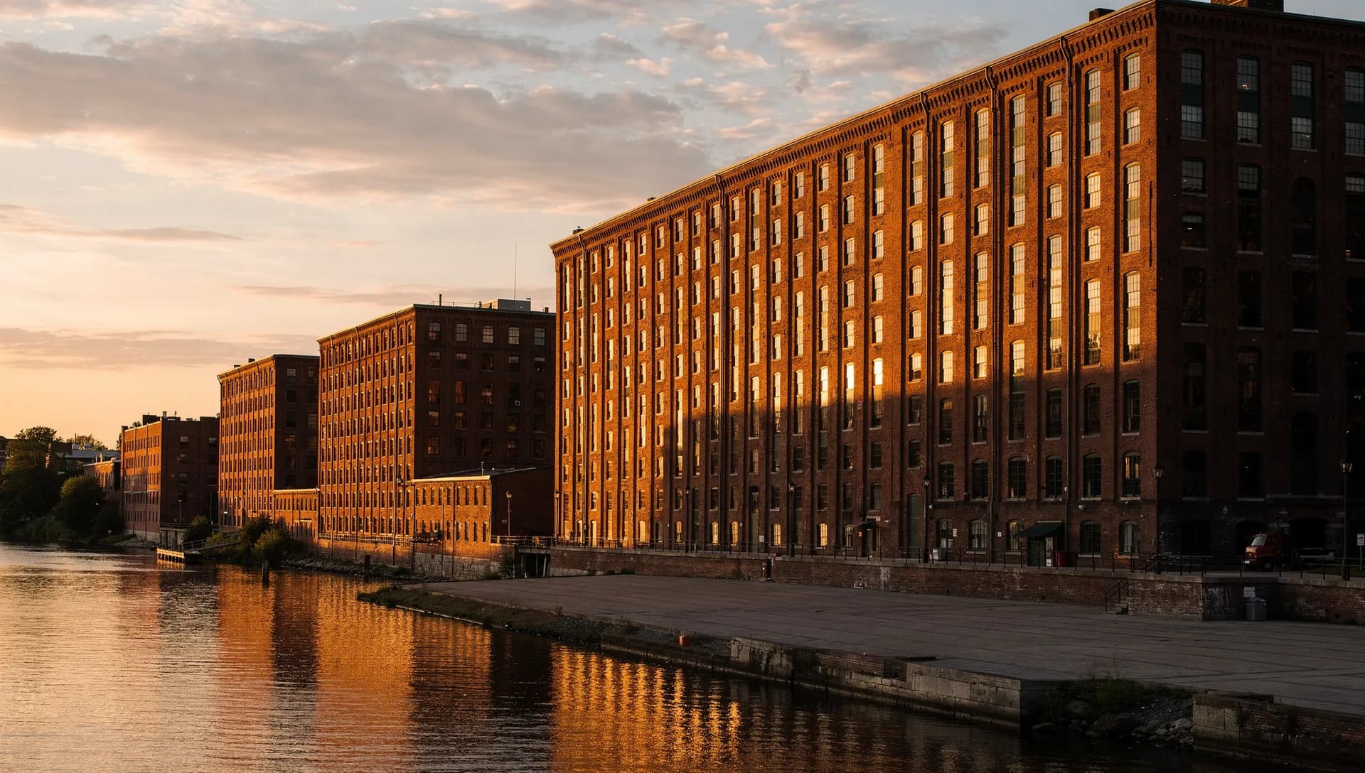 The brick Amoskeag Millyard buildings lining the Merrimack River in Manchester, New Hampshire, under an evening sky.